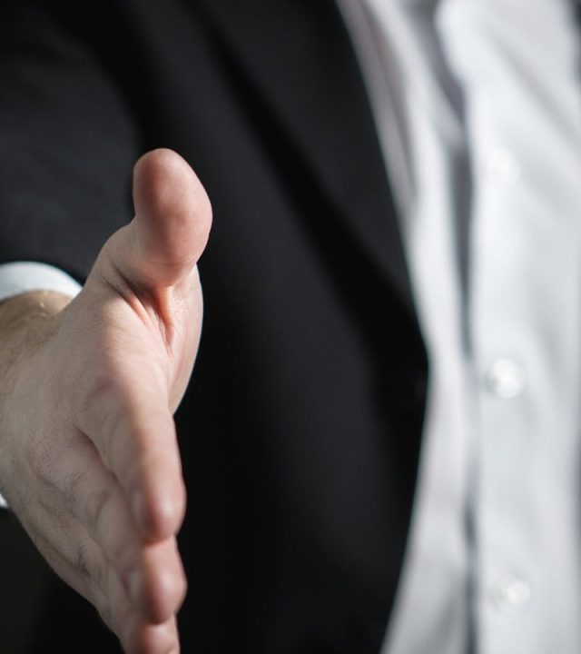 Close-up of a businessman extending hand for a handshake, symbolizing agreement and partnership.